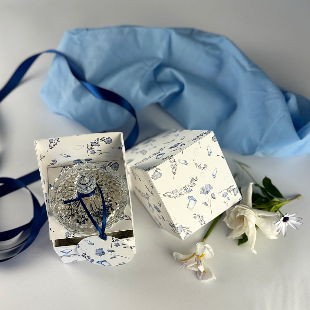 top down view of angelic whispers candle in product box, art deco crystal lid with navy ribbon and label