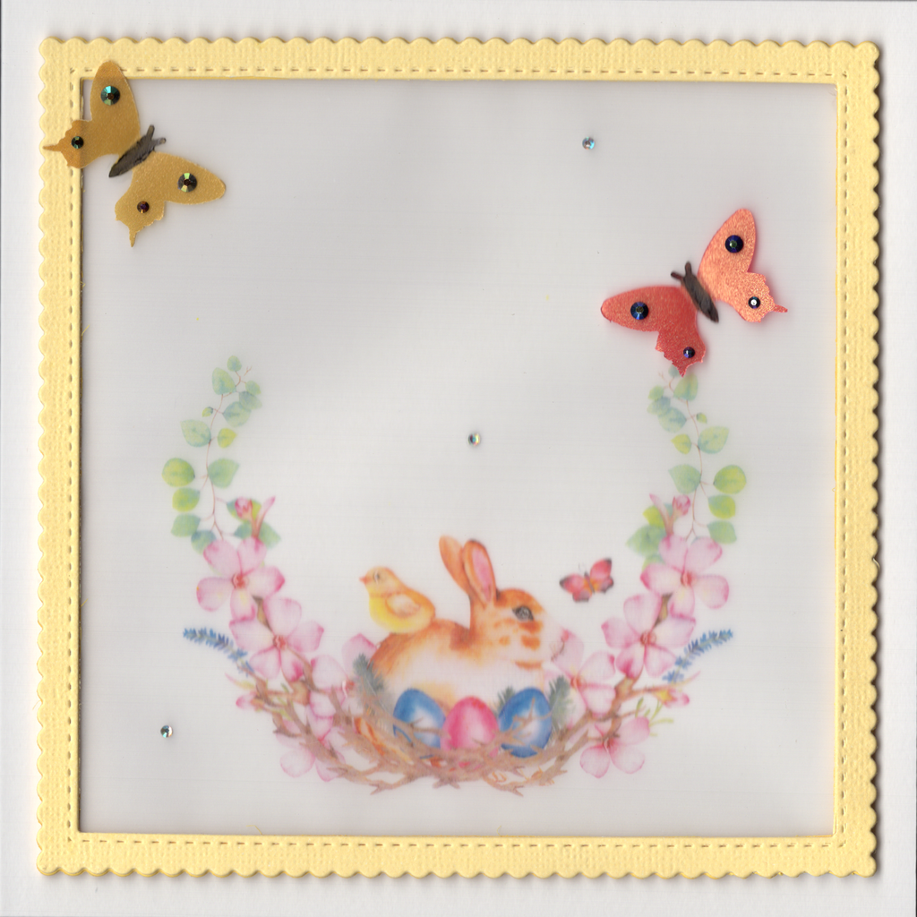 This beautiful card is printed on heavy Eggshell textured card stock. It features a raised framed panel of vellum which is secured in a yellow scalloped frame. A cute bunny with a chick on its back sits behind Easter Eggs nestled in a wreath of flowers. Two butterflies with jewels on their wings sit proudly. Glossy accents on the eyes of the bunny and chick and in the centre of the flowers provide the finishing touches to this delicate card.