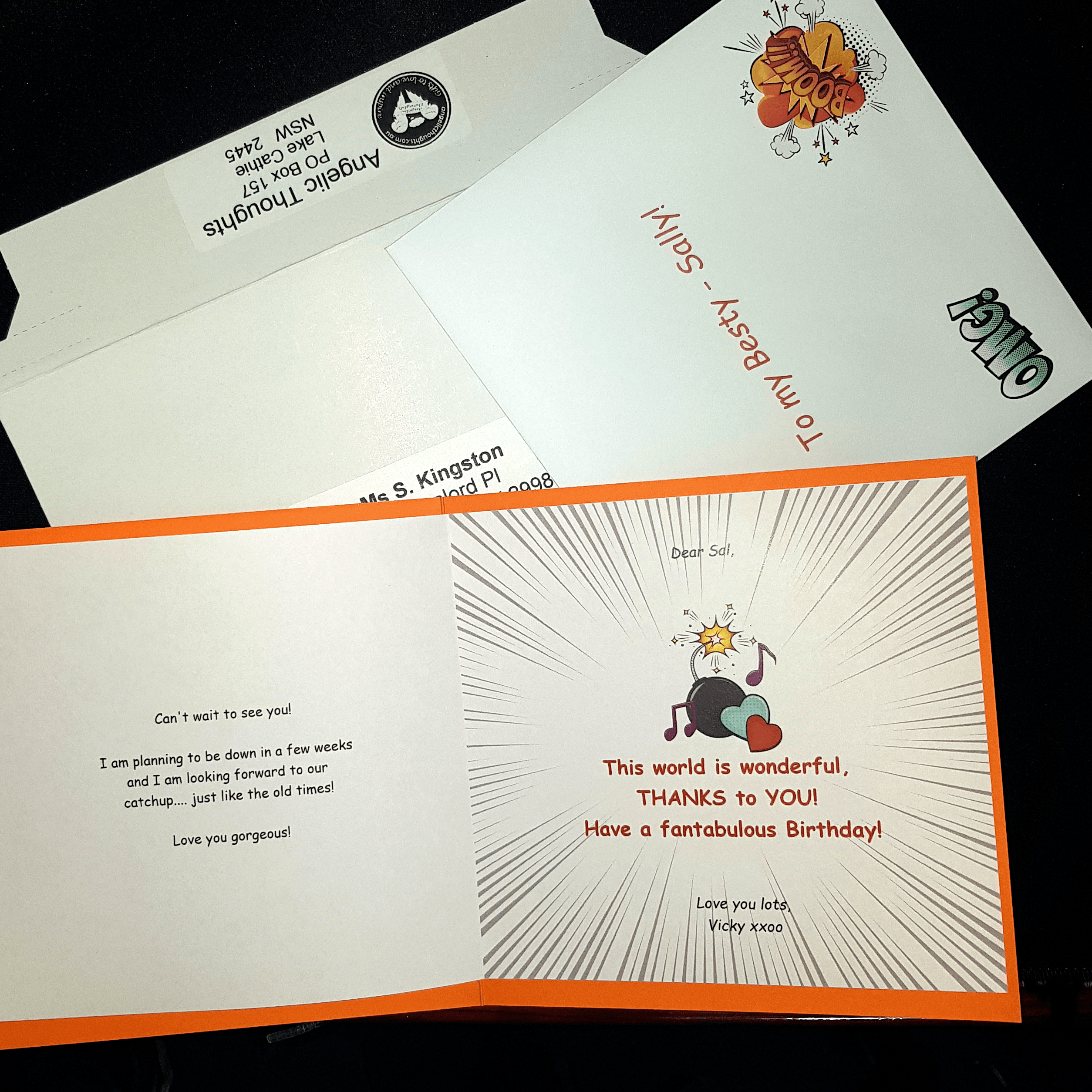 An open card which has been customised laying on an envelope and rigid mailer