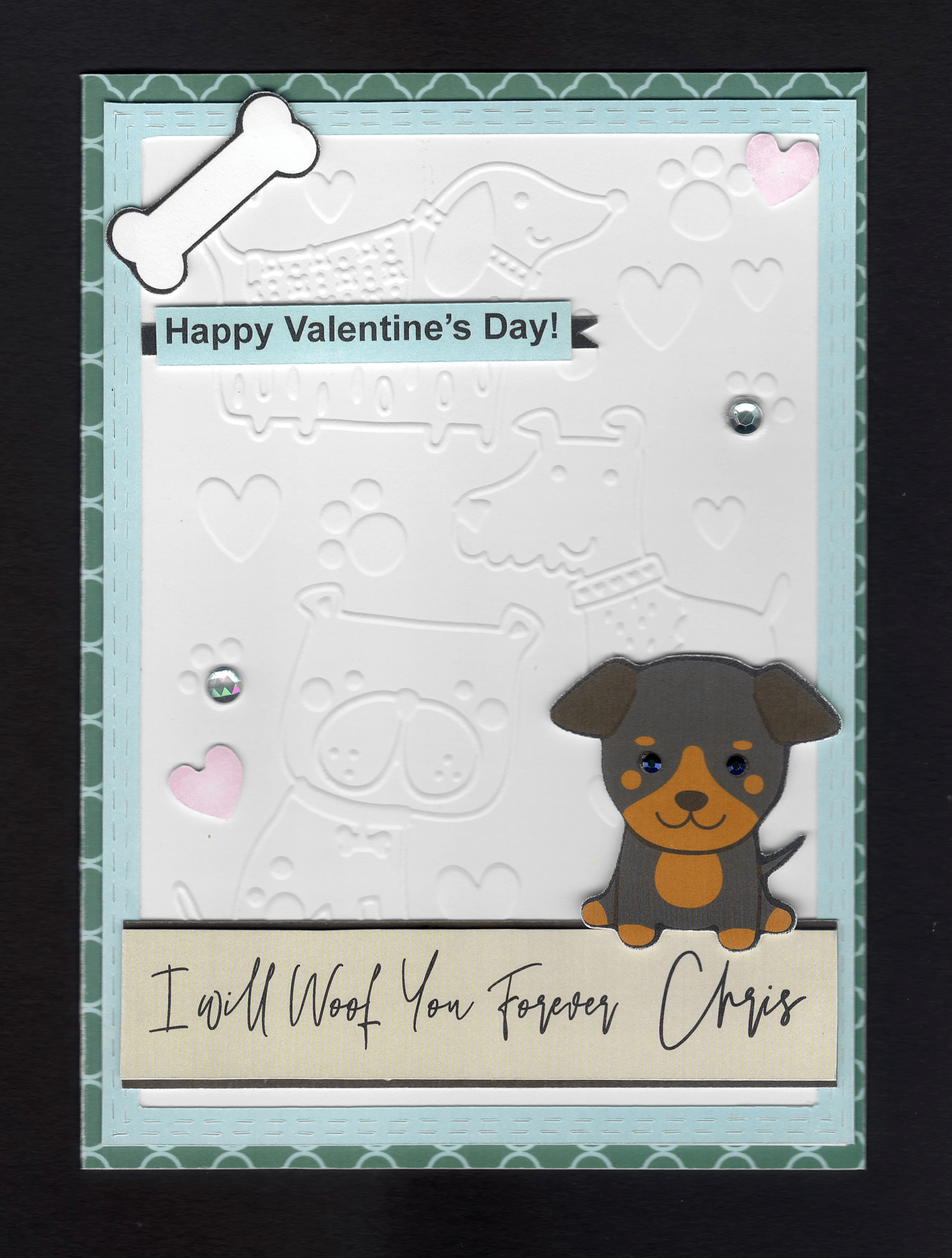 A beautiful card with embossed cartoonlike impressions of various types of dogs, pawprints and hearts on white cardstock forming the background, with gems in two of the paw prints, a cute dogof your choise sits on a beige/blacksentiment strip with the recipients name. A bone and two pink hearts sit proud. A blue faux stitched frame sits over and a teal/light blue moroccan style background completes the look