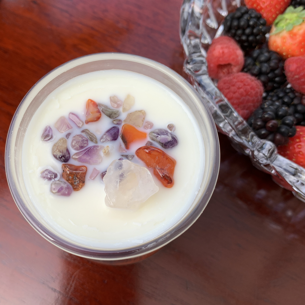 Berry Delightful Soy Wax candle in a clear glass container embellished with Clear Quartz, Amethyst and Carnelian Chips. Part of a crystal bowl containing raspberries, blackberries, strawberries is visible in the top right corner
