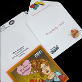 Front of customised card, and open envelope lying on addressed rigid mailer
